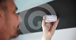 Person's Hand Installing Smoke Detector On Ceiling Wall