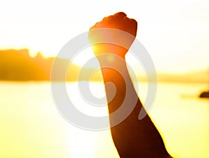 A person's hand making a fist with the sunset in the background - concept of strength