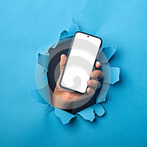Hand Holding Smartphone Through Torn Blue Paper photo