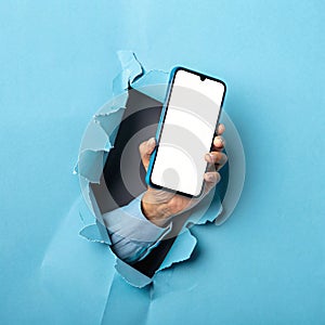 Hand Holding Smartphone Through Torn Blue Paper photo