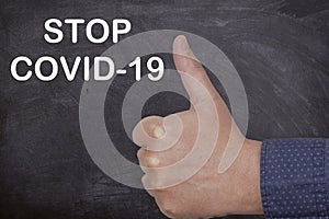 Person's hand showing thumbs up with Stop COVID-19 text - global pandemic concept