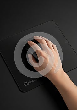 A person's hand using a black computer mouse on a matching black mouse pad. The surface appears