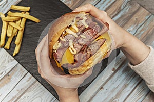 Person's hands holding a beastly three meat burger with lots