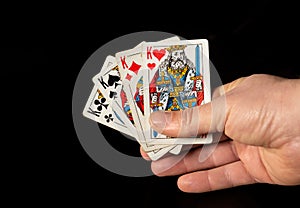 Person`s hands are holding playing cards four kings close up on black background