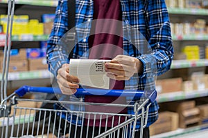 a person's hands holding a shopping list paper sheet and check buying products in grocery store