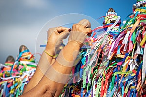A person's hands are tying a souvenir ribbon on the railing of the Senhor do Bonfim church in the city of Salvador, Bahia