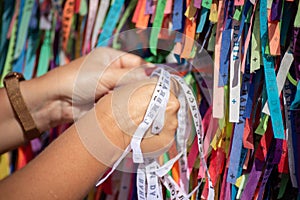 A person's hands are tying a souvenir ribbon on the railing of the Senhor do Bonfim church in the city of Salvador, Bahia