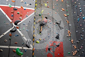 Person with Safety Harness and Climbing Shoes is attached to a Rope and Climbing up a Wall in an Indoor Climbing Hall