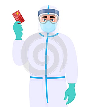 Person in safety protection suit, medical mask, glasses and face shield showing credit, debit, ATM card. Doctor or physician