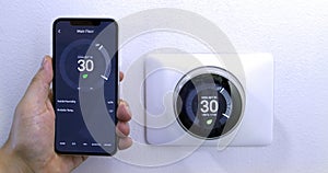 A person saving energy, air conditioner, with a smart phone using a wireless Thermostat on a white wall.