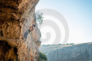 Person is scaling a cliff face, ascending the rock wall with ropes and equipment
