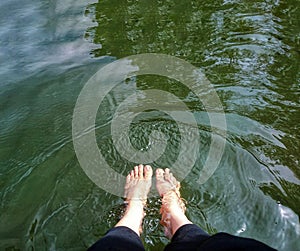 Person seated on a boulder in a lake, with their feet submerged in the cool, refreshing water