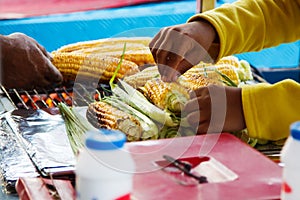 Person selling grilled corn outdoors in summer.