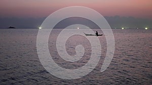 Person on shallop between lights of fishing ships in sea at sunset. Picturesque view of silhouette shipping on shallop