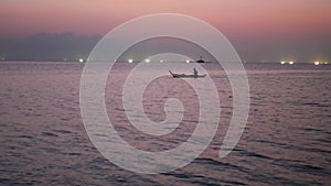 Person on shallop between lights of fishing ships in sea at sunset. Picturesque view of silhouette shipping on shallop