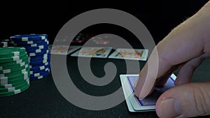 Person showing his deck at the poker game. Card player checks his hand, two aces in, chips in background on green