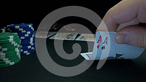 Person showing his deck at the poker game. Card player checks his hand, two aces in, chips in background on green