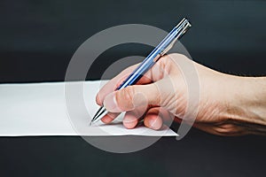 Person sign document and hand holds blue pen on dark background