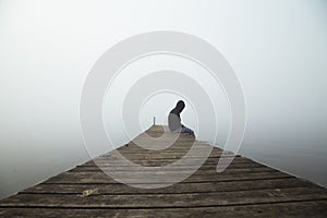 Person sitting on dock early morning with fog in the sky