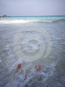 A person sitting on sandy beach in water. Bare feet.
