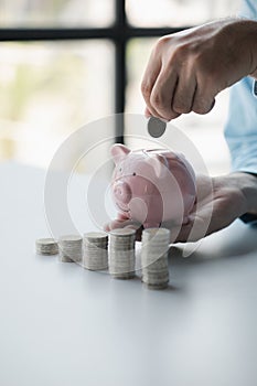 Person with stack of coins and piggy bank, saving money concept for future use.