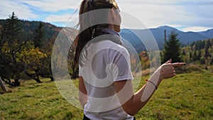 A person standing in front of a field. Young tourist woman dances in a clearing against the backdrop of the mountains