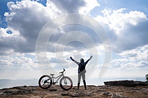 A person standing with hands up beside a bicycle on rocky mountain