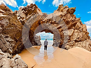 A person standing near an arched rock admiring the view