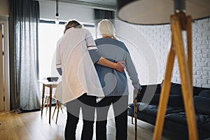 A person standing in a room. Woman walking with nurse old age home