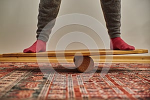 Person standing on a wooden balance board in the living room. Home exercises during the lockdown