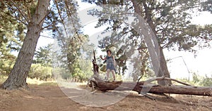 A person stands on a fallen tree trunk in a forested area