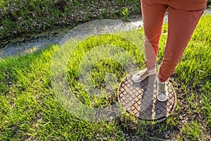 A person stands on a rusty manhole cover near gutter with water