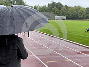 Person stands with an umbrella in the rain at the edge of a sports field