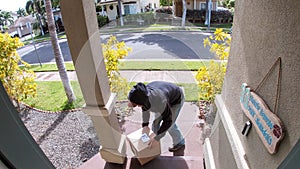 Person stealing delivery package from porch steps, surveillance camera view