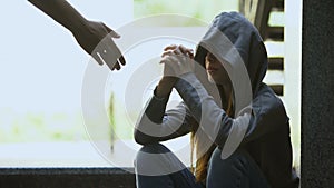 Person stretching helping hand to lonely depressed teen girl, support and aid