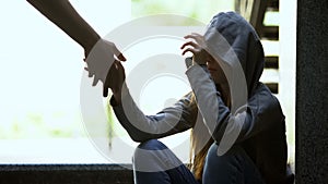 Person stretching helping hand to lonely depressed teen girl, support and aid