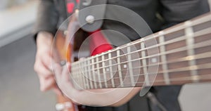 Person strikes the strings of electric guitar holding a pick in hand, close up, camera descends down along the guitar