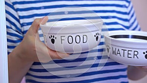 Person in a striped shirt holding two bowls labeled FOOD and WATER for pets, symbolizing care and preparation for