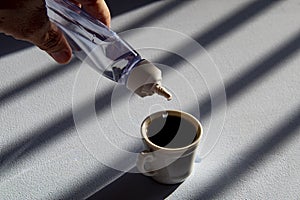 person sweetening coffee with liquid sweetener