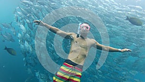 Person swimming among shoal of jack fish in tulemben in Bali, Indonesia