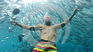 Person swimming among shoal of jack fish in tulemben in Bali, Indonesia