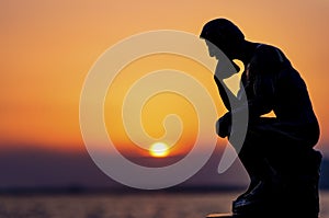 A person thinks by the sea at sunset