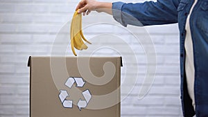 Person throwing banana peel into trash bin, organic waste sorting, awareness