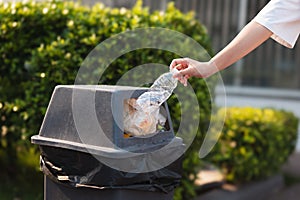 person is throwing plastic bottle into a trash can