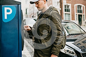 A person or a tourist pays for car parking in a street parking machine