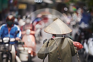 Person with traditional conical hat against traffic motorbikes on busy street