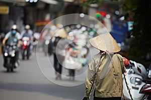 Person with traditional conical hat against traffic motorbikes on busy street