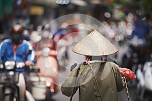 Person with traditional conical hat against traffic motorbikes on busy street photo