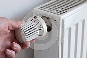 person turning down thermostat on heater to save energy
