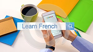 Person typing learn French phrase on smartphone search bar, online education